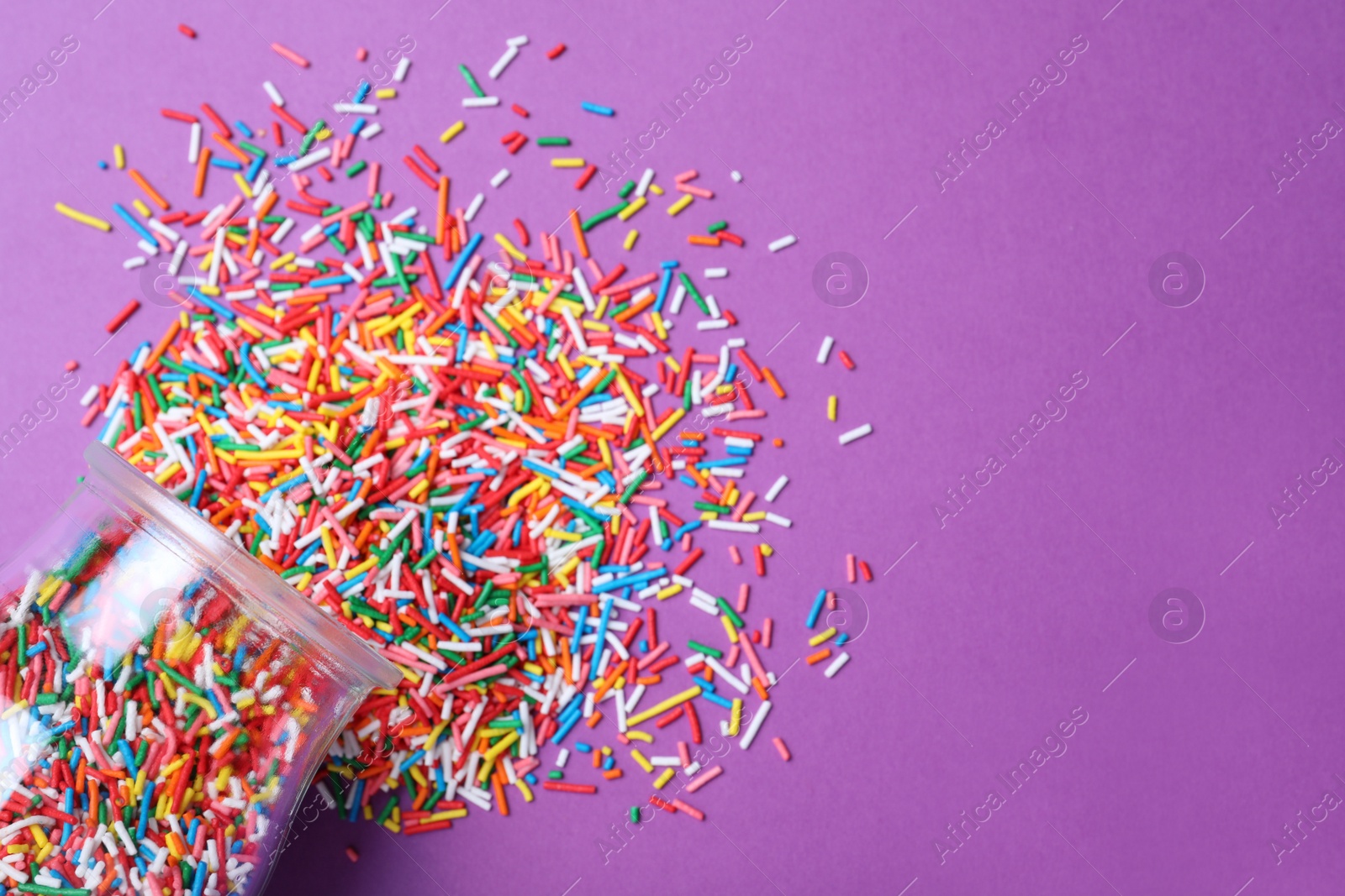 Photo of Jar with colorful sprinkles and space for text on purple background, flat lay. Confectionery decor