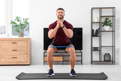 Athletic man doing exercise with elastic resistance band on mat at home