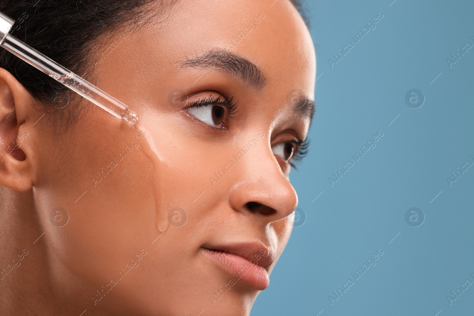 Photo of Beautiful woman applying serum onto her face on blue background, closeup. Space for text