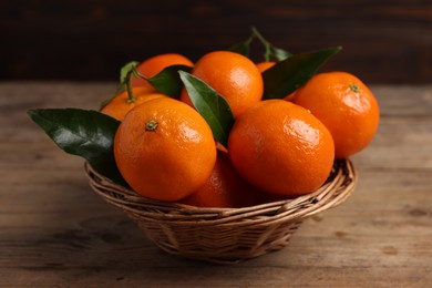 Delicious tangerines with leaves in wicker basket on wooden table, closeup