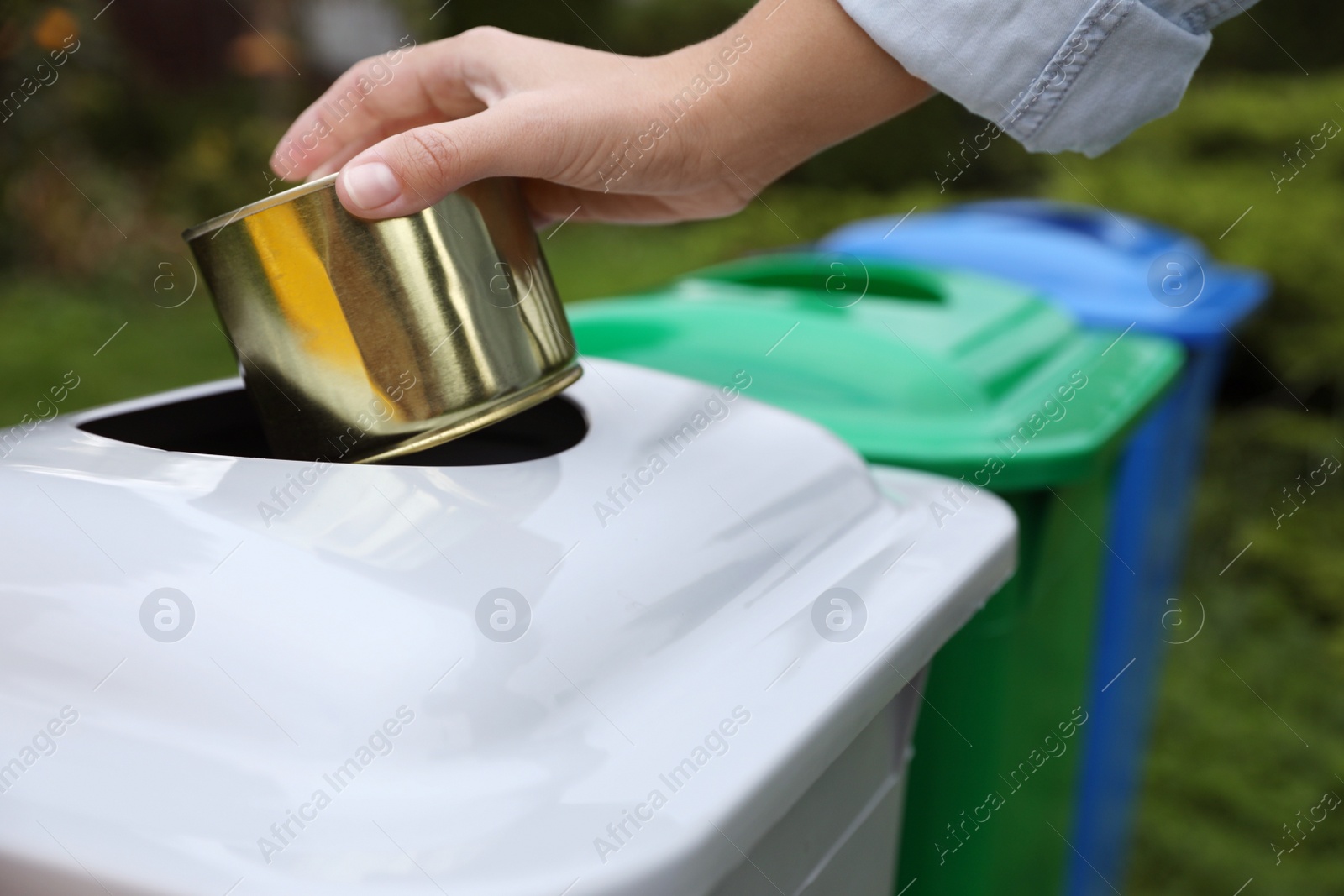 Photo of Woman throwing tin can into recycling bin outdoors, closeup