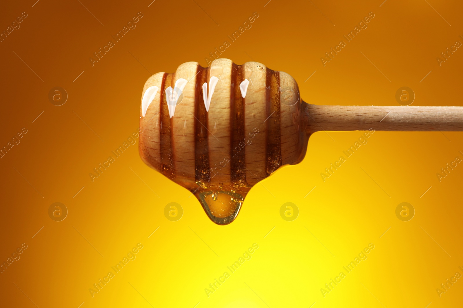 Photo of Pouring honey from dipper against golden background, closeup