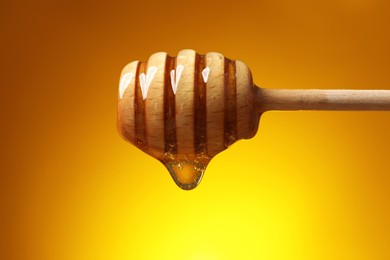 Photo of Pouring honey from dipper against golden background, closeup