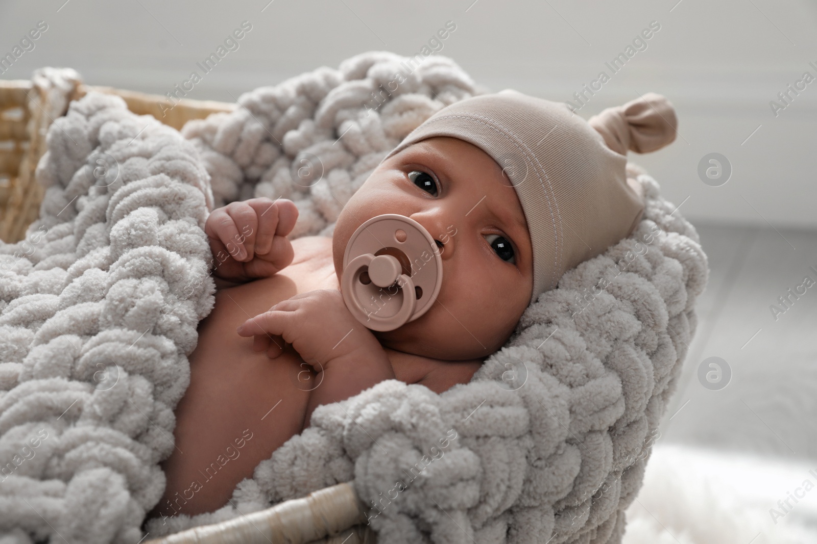 Photo of Adorable newborn baby with pacifier in wicker basket indoors