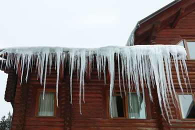 House with icicles on roof, low angle view. Winter season