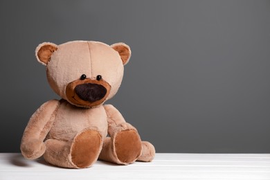Cute teddy bear on white wooden table near black wall, space for text