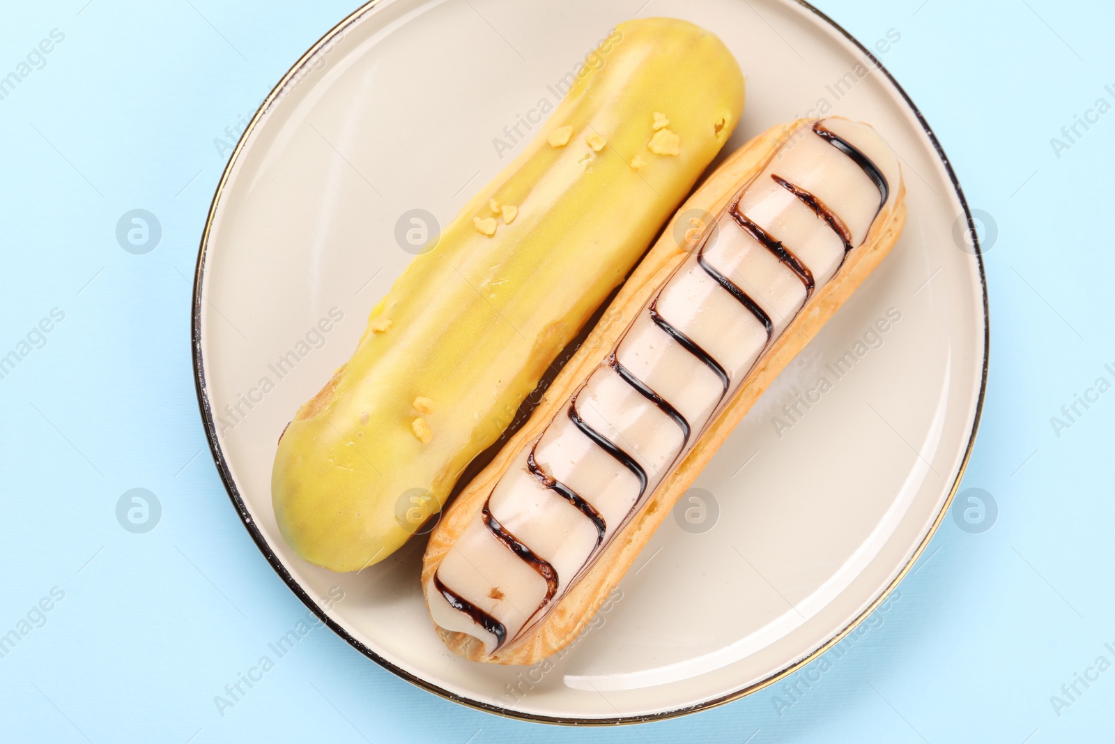 Photo of Delicious eclairs covered with glaze on light blue background, top view