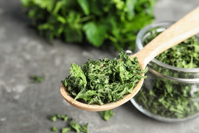 Spoon and jar of dried parsley on grey table, closeup