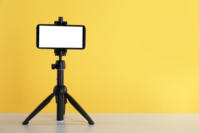 Photo of Smartphone with blank screen fixed to tripod on white table against yellow background. Space for text