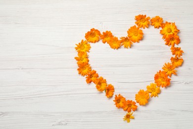 Heart of beautiful calendula flowers on white wooden table, top view. Space for text