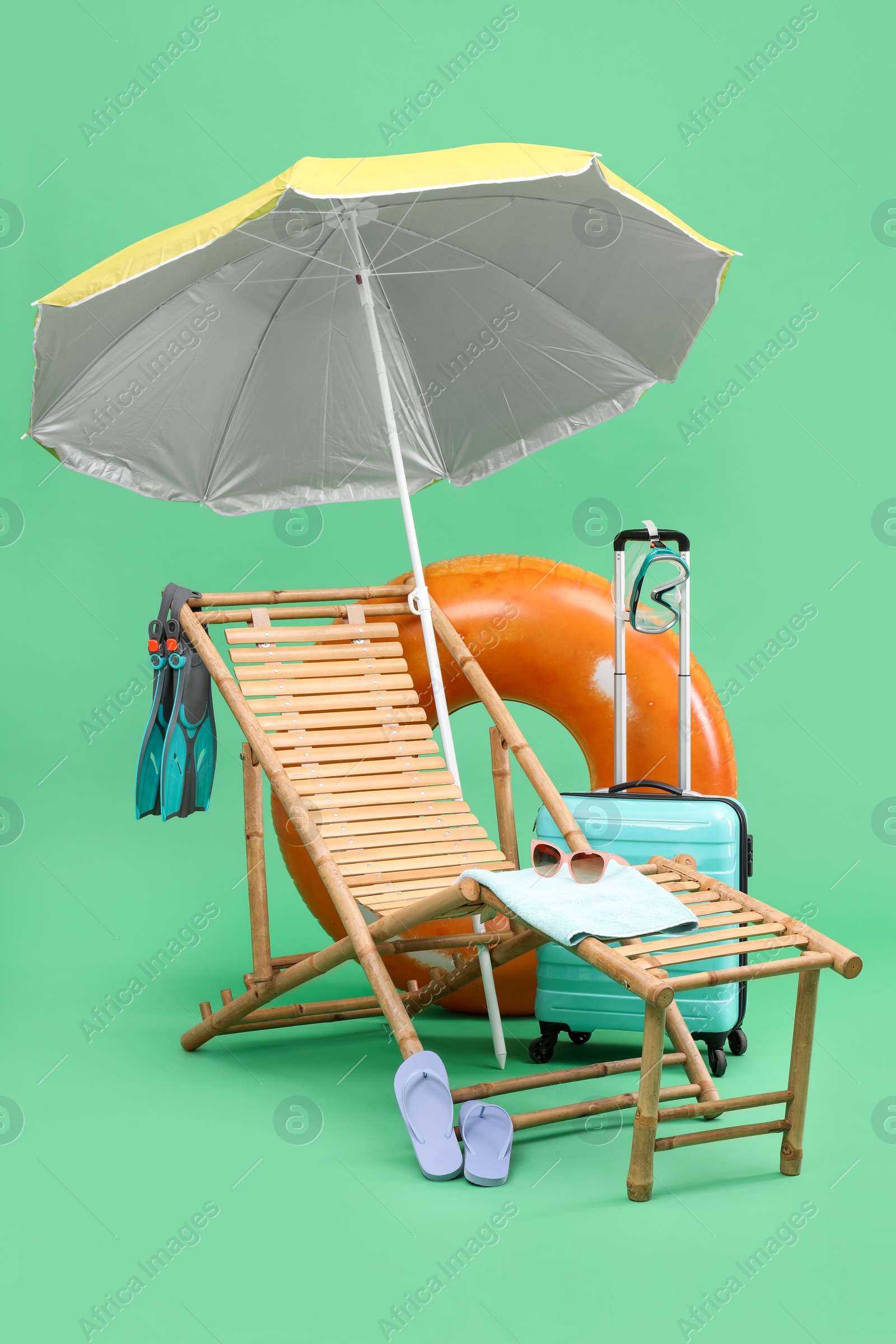 Photo of Deck chair, umbrella, suitcase and beach accessories against green background. Summer vacation