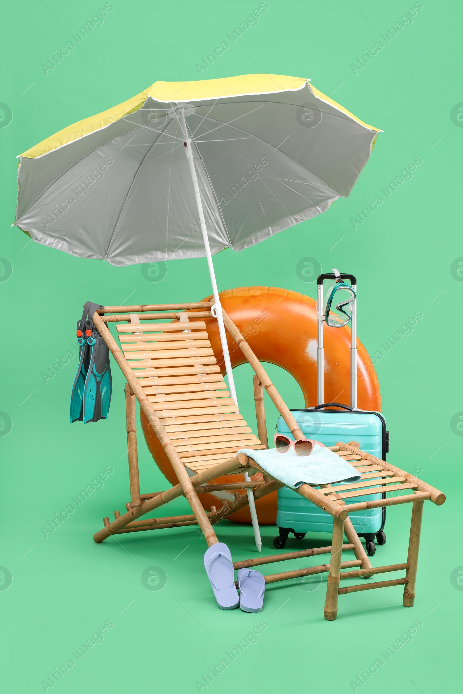Deck chair, umbrella, suitcase and beach accessories against green background. Summer vacation Photo of Deck chair, umbrella, suitcase and beach accessories against green background. Summer vacation