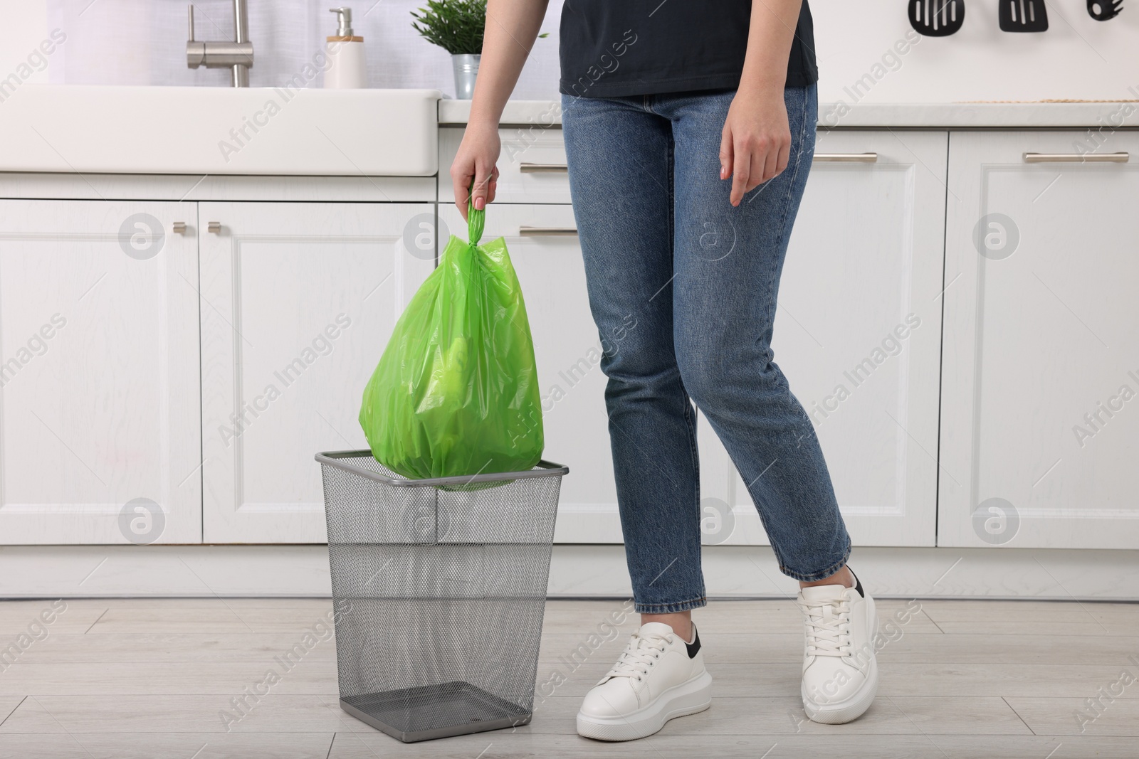 Photo of Woman taking garbage bag out of trash bin in kitchen, closeup