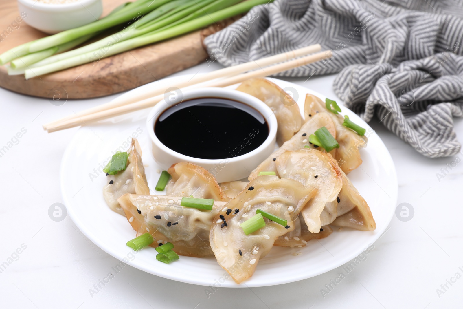 Photo of Delicious gyoza (asian dumplings) with green onions, soy sauce and chopsticks on white table, closeup