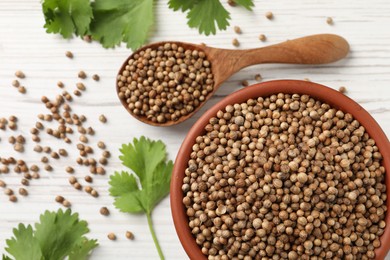 Photo of Dried coriander seeds in bowl, spoon and green leaves on wooden table, flat lay