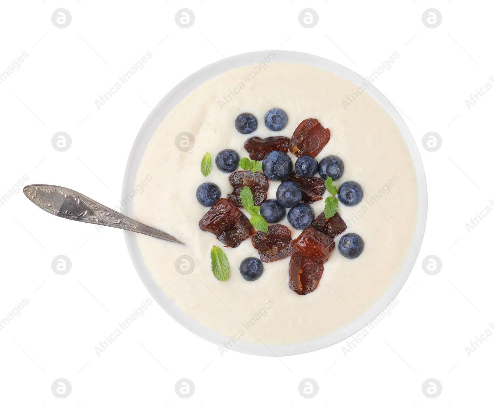 Photo of Delicious semolina pudding with blueberries, dates, mint and spoon in bowl isolated on white, top view