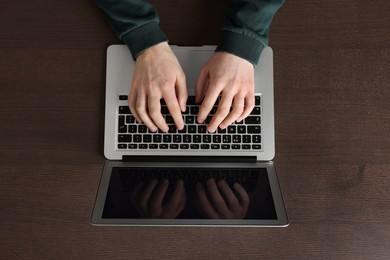 Man working with laptop at wooden table, top view