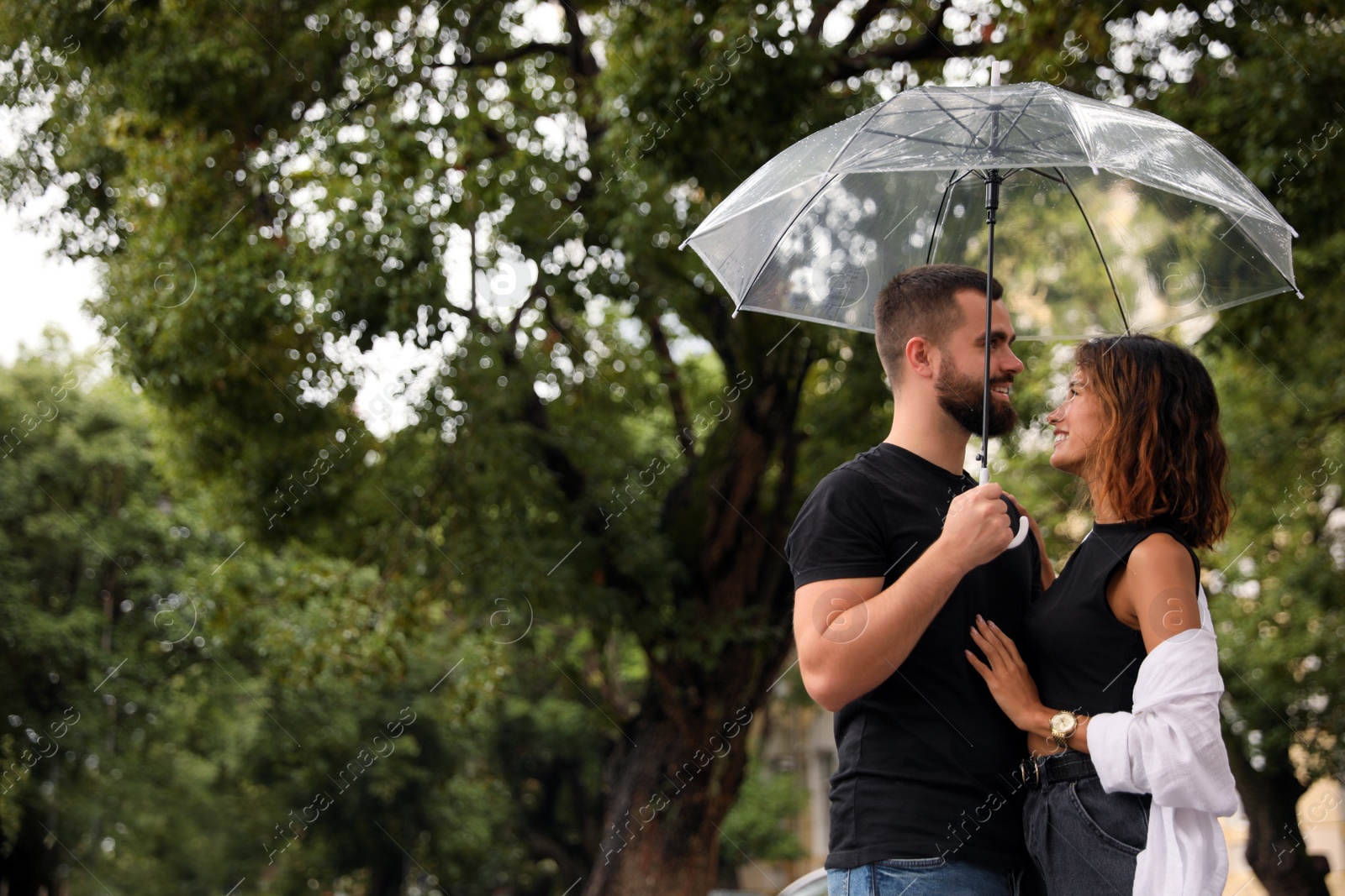 Photo of Young couple with umbrella enjoying time together under rain outdoors, space for text