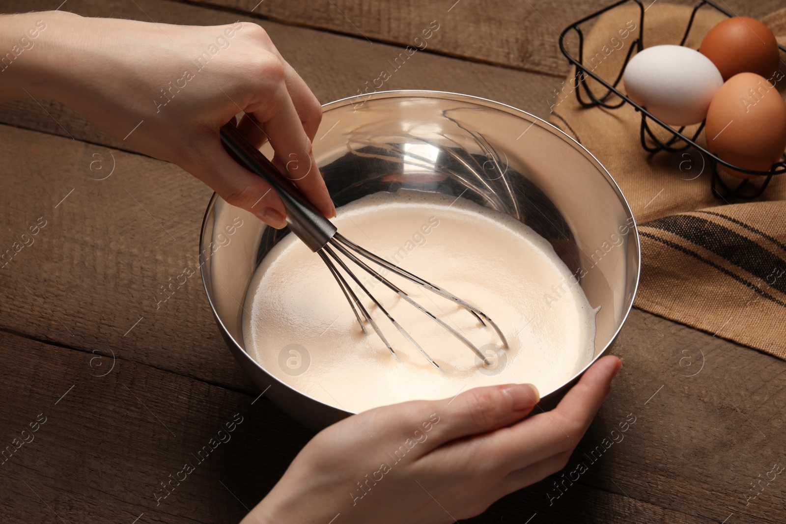 Photo of Woman whipping ingredients with whisk at wooden table, closeup. Cooking delicious eggnog