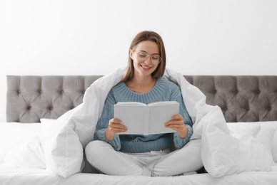 Photo of Young woman in warm sweater reading book on bed at home