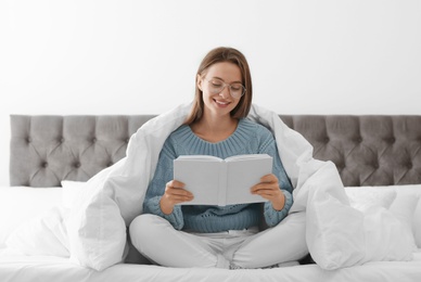 Young woman in warm sweater reading book on bed at home