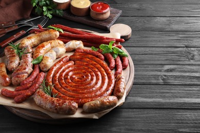 Different delicious sausages with herbs on black wooden table, space for text. Assortment of beer snacks