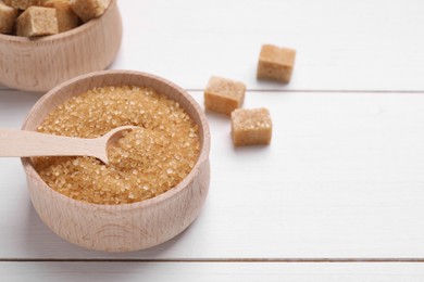 Photo of Bowls and spoon with different types of brown sugar on white wooden table, closeup. Space for text