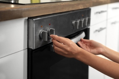 Photo of Woman using electric oven in kitchen, closeup