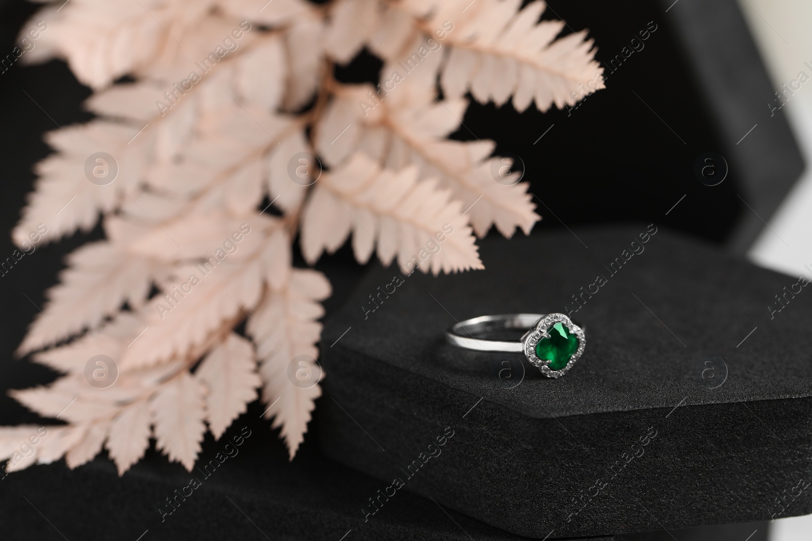 Photo of Beautiful ring with green gemstone on black podium, closeup. Luxury jewelry