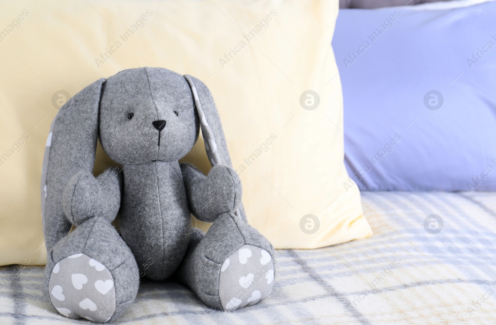 Photo of Cute toy rabbit sitting on bed indoors. Space for text