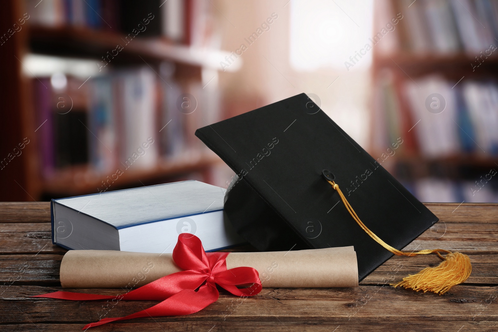 Image of Graduation hat, book and diploma on wooden table in library