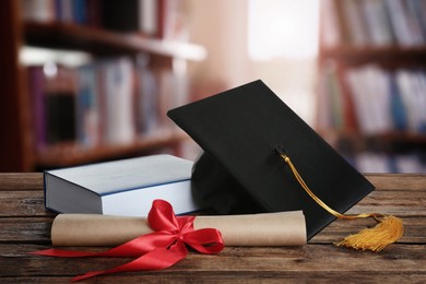 Image of Graduation hat, book and diploma on wooden table in library