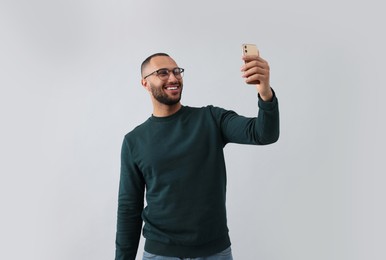 Photo of Smiling young man taking selfie with smartphone on grey background