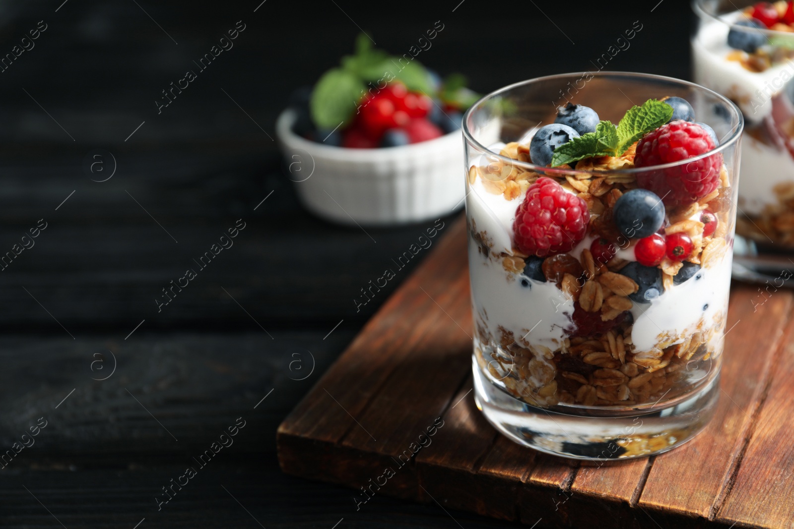 Image of Yummy dessert with granola, yogurt and berries on dark wooden table, space for text