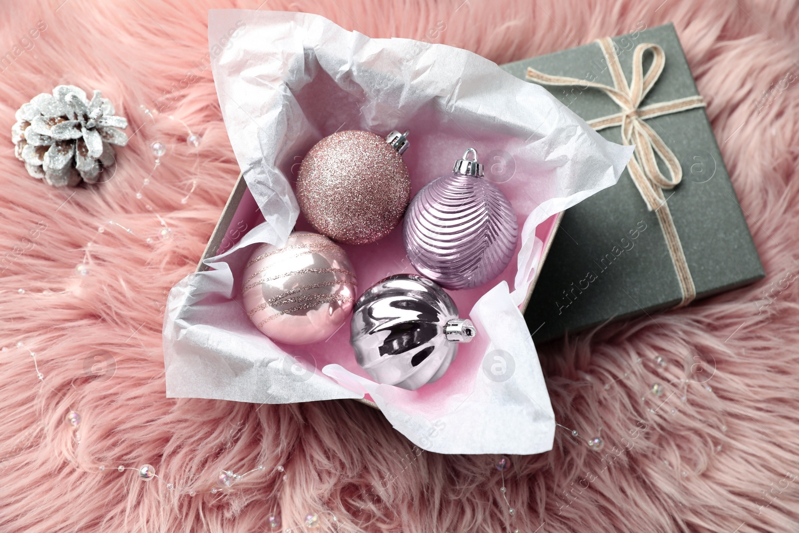 Photo of Beautiful Christmas baubles in box on pink faux fur, flat lay