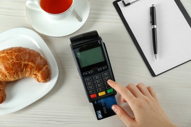 Woman with credit card using modern payment terminal at white table, top view
