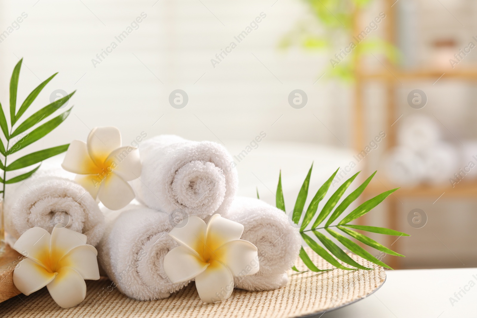 Photo of Spa composition. Towels, plumeria flowers and palm leaves on white table in bathroom