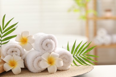 Photo of Spa composition. Towels, plumeria flowers and palm leaves on white table in bathroom