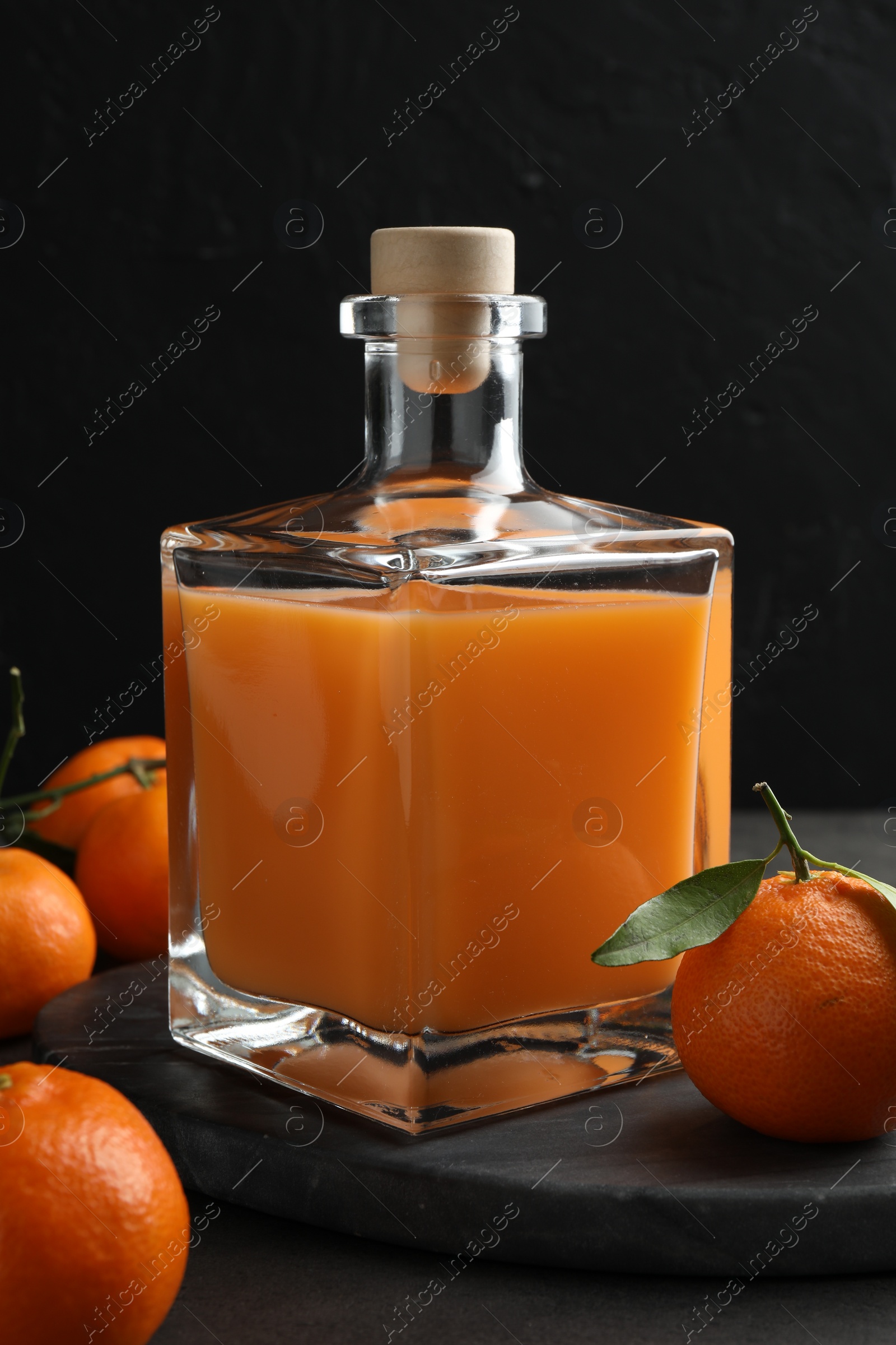 Photo of Delicious tangerine liqueur in glass bottle and fresh fruits on grey table