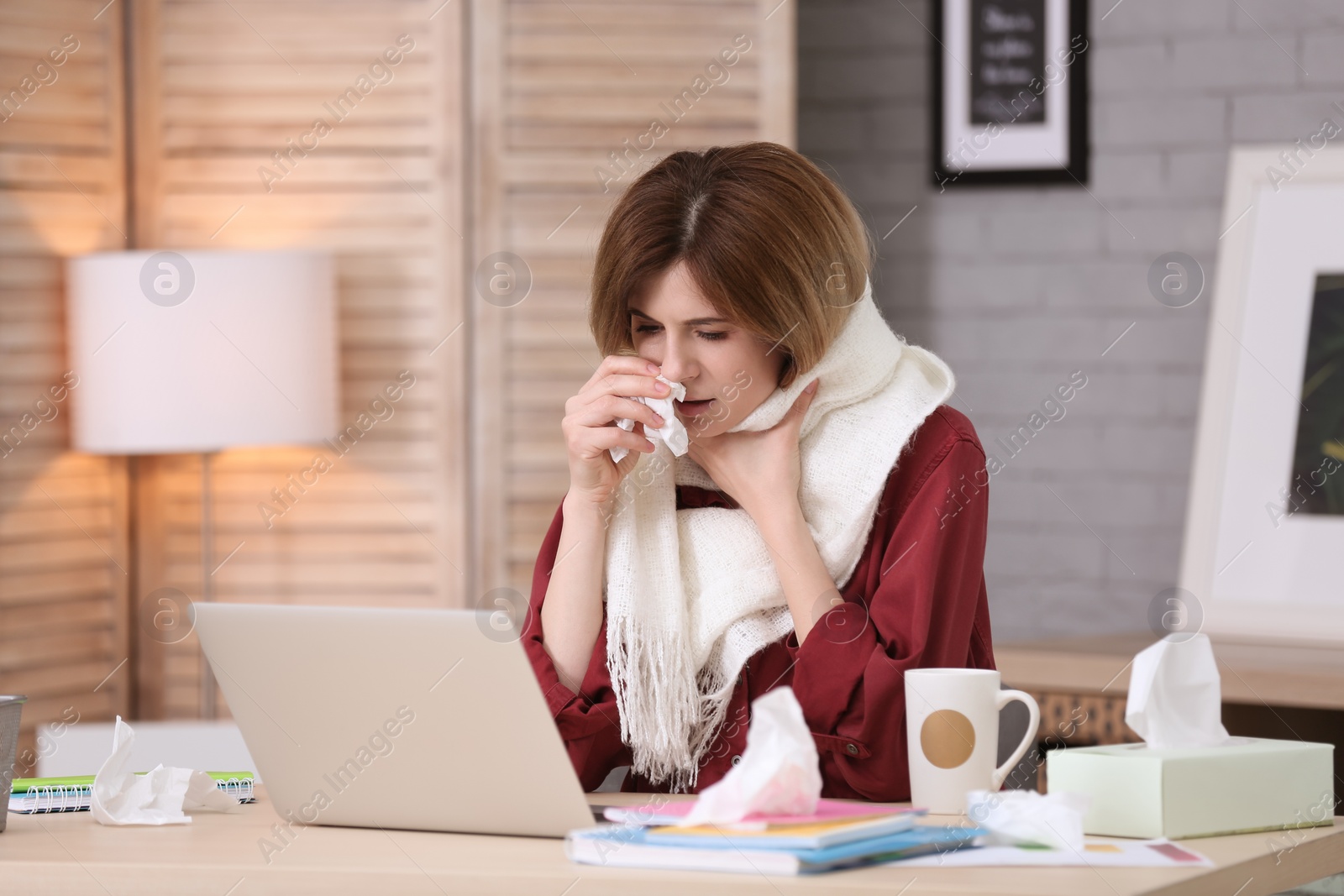 Photo of Sad woman with tissue suffering from cold while working with laptop at table