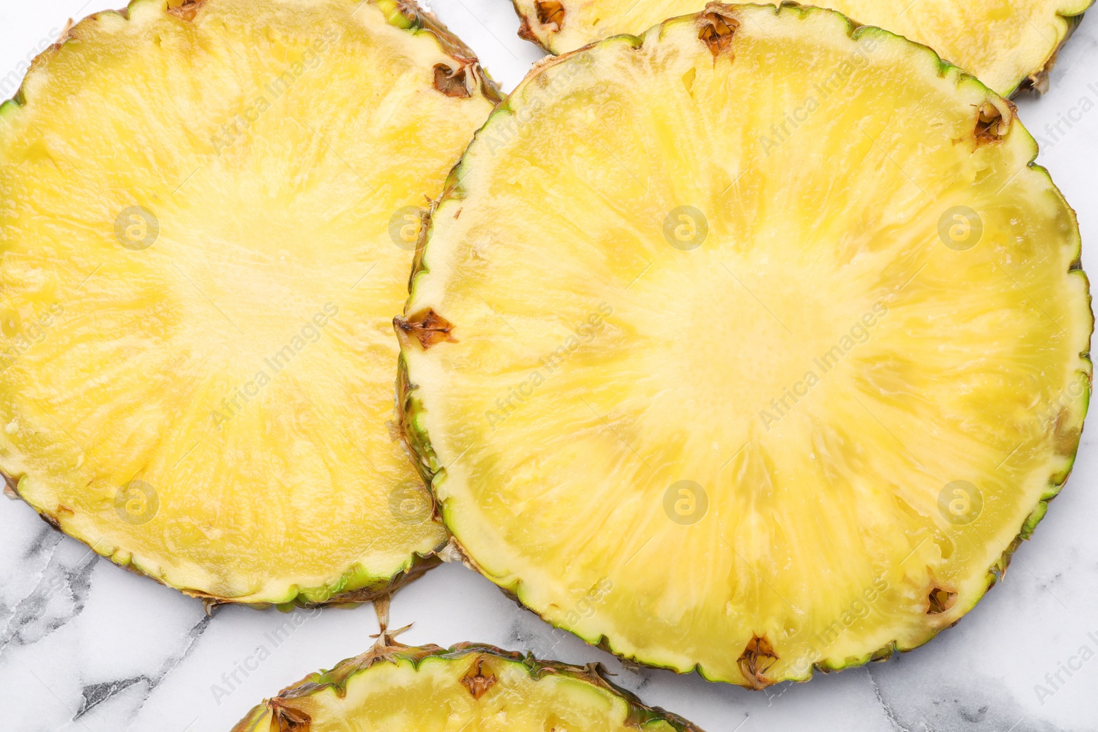 Photo of Slices of tasty ripe pineapple on white marble table, flat lay