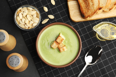 Photo of Delicious broccoli cream soup with croutons served on black table, flat lay