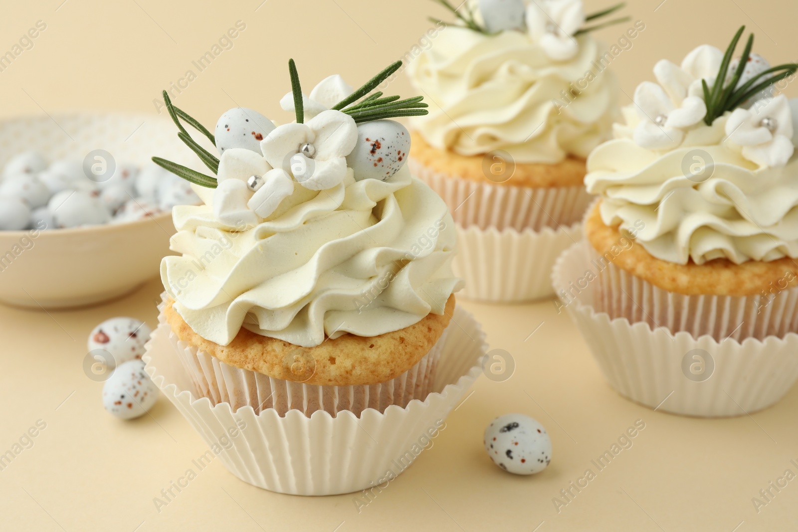 Photo of Tasty Easter cupcakes with vanilla cream and candies on beige background, closeup