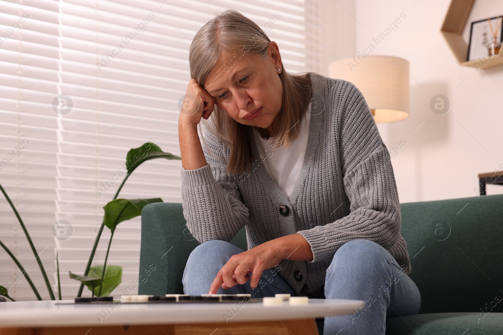 Photo of Thoughtful senior woman playing checkers at home