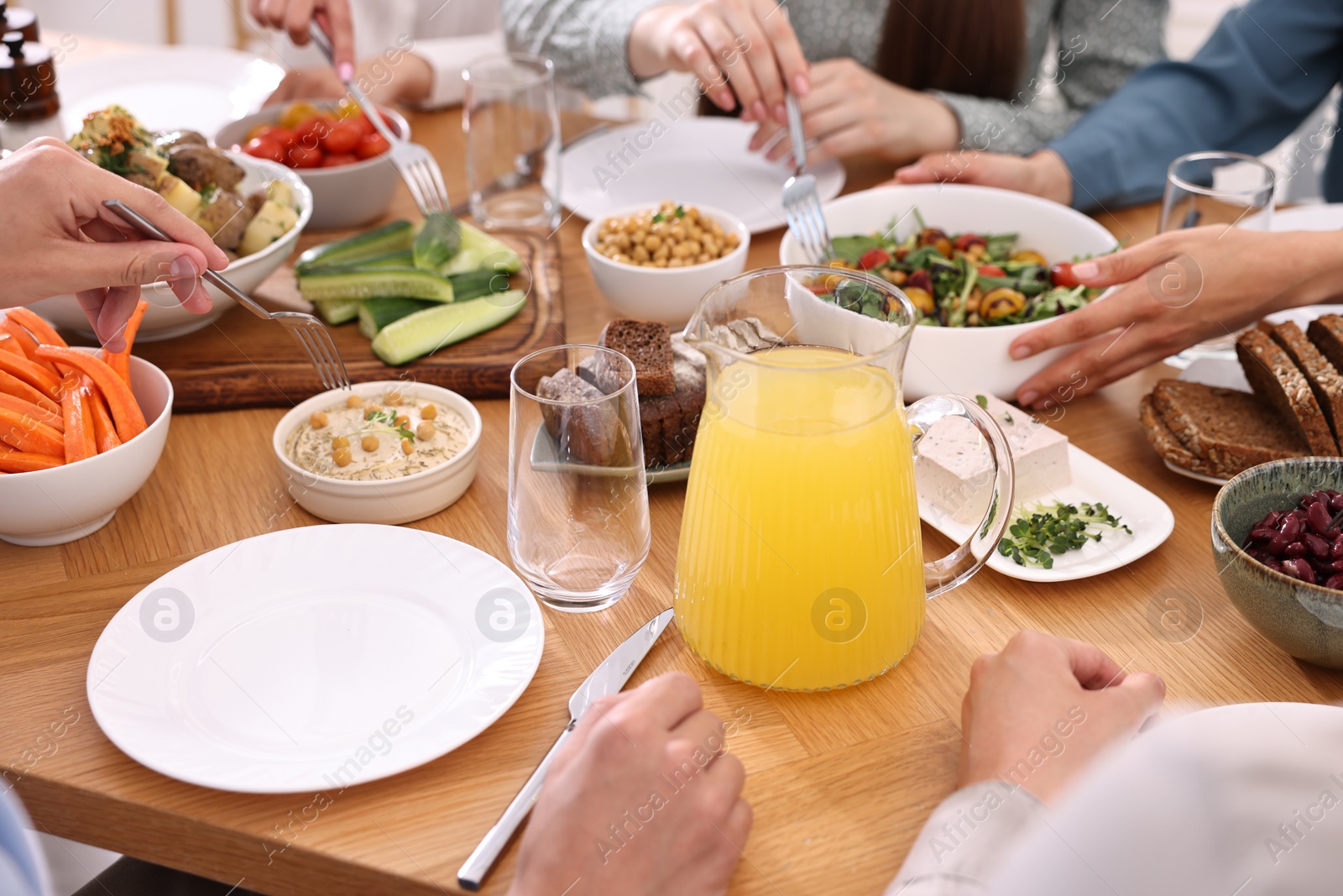 Photo of Friends eating vegetarian food at wooden table indoors, closeup