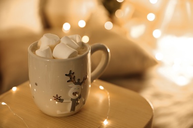 Photo of Cup of hot drink with marshmallows on small wooden table, space for text. Christmas atmosphere