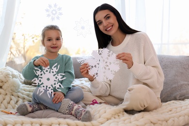Photo of Mother and daughter with paper snowflakes near window at home
