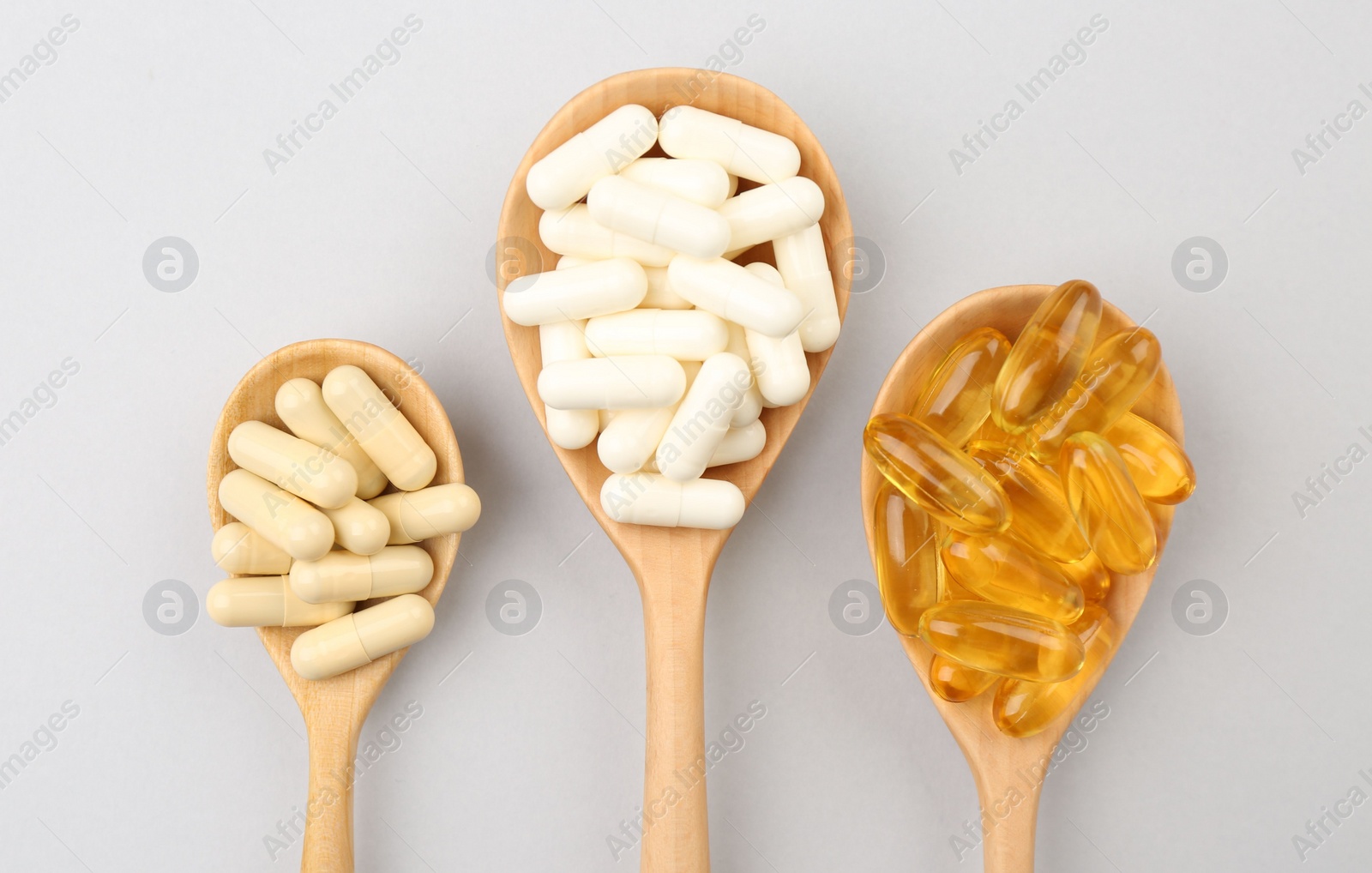 Photo of Wooden spoons with different vitamin capsules on light grey background, flat lay