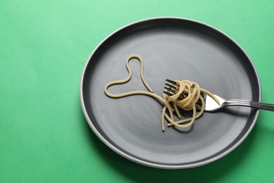 Photo of Heart made of tasty spaghetti and fork on green background. Space for text