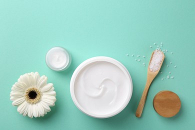 Photo of Moisturizing cream in open jars, sea salt and gerbera flower on turquoise background, flat lay. Body care products